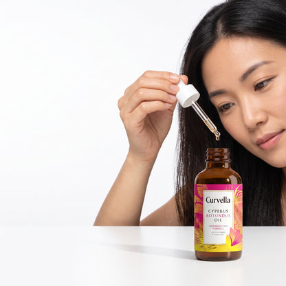 lifestyle: A new photorealistic photograph composed from scratch. An East Asian woman in her 30s is gently squeezing the product's dropper, applying the oil to her hair/scalp. Her hand and a portion of her head/hair are visible, along with the product bottle on a pristine, seamless pure-white sweep (RGB 255,255,255) that dissolves smoothly into the background. The product and model interaction fill approximately 60% of the frame, positioned to the right third. The scene is lit by broad soft wraparound diff…