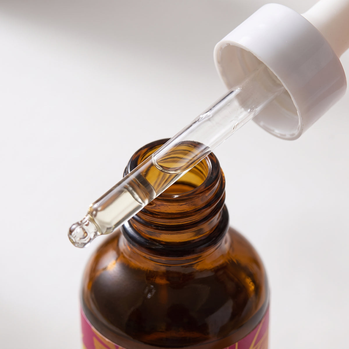 detail: NEW photorealistic photograph. A tight, intimate macro shot focuses on the upper section of the product, specifically highlighting the glass dropper and the rich amber hue of the bottle's neck. The background is a minimalist, softly blurred white surface, reminiscent of a studio sweep. Soft, diffused light gently grazes the bottle from the upper-right, emphasizing subtle textures and reflections on the glass dropper. The mood is clean and refined. Captured with a 100mm macro lens at f/2.8, achievin…